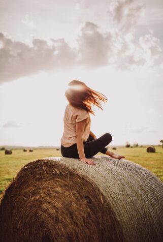 A closeup shot of a lonely female sitting on a grass heap on a bright sunny day