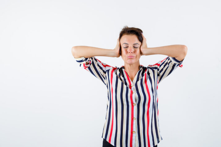 mature woman pressing hands on ears, closing eyes in striped shirt and looking calm , front view.